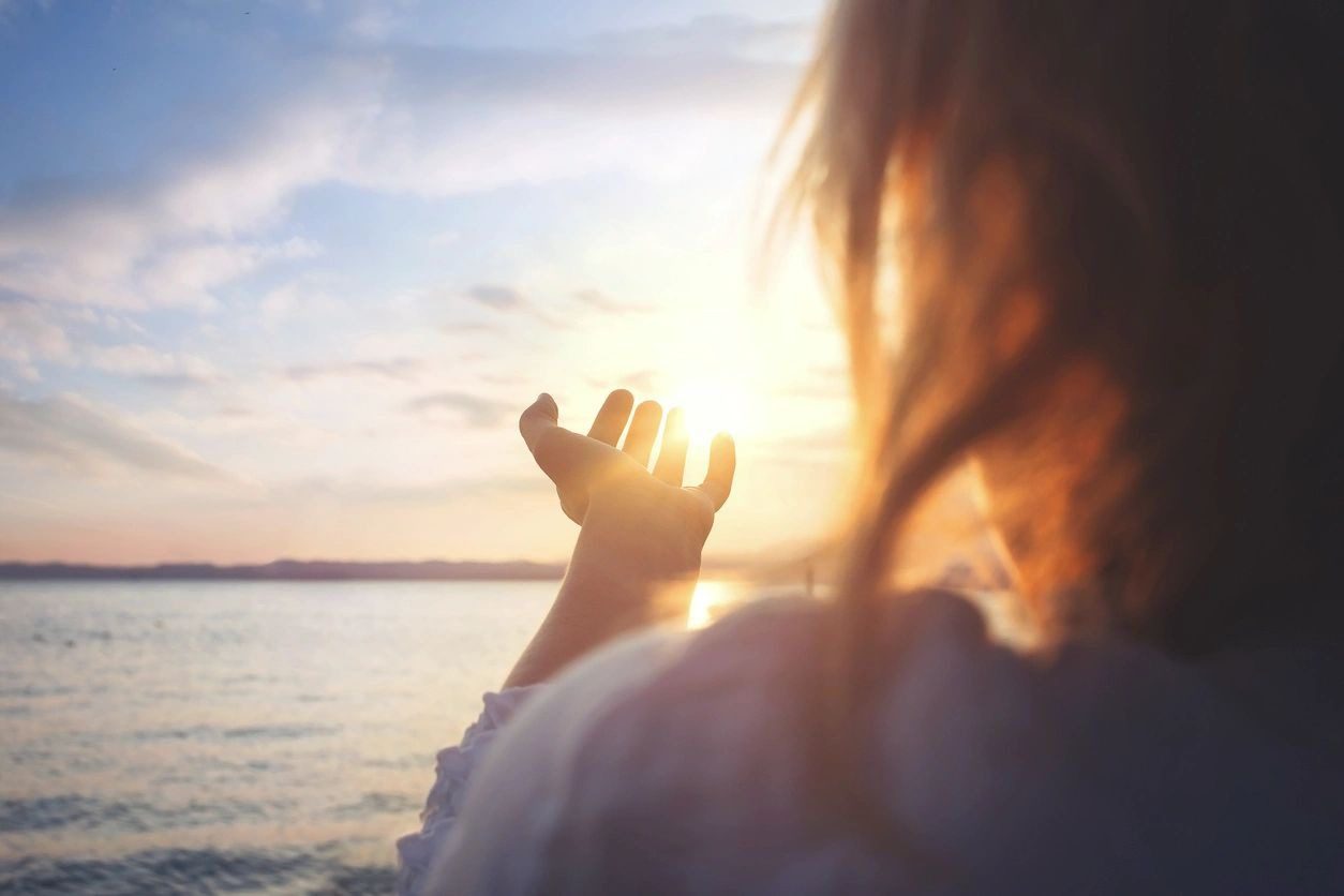 A person is holding their hand out to the sun.